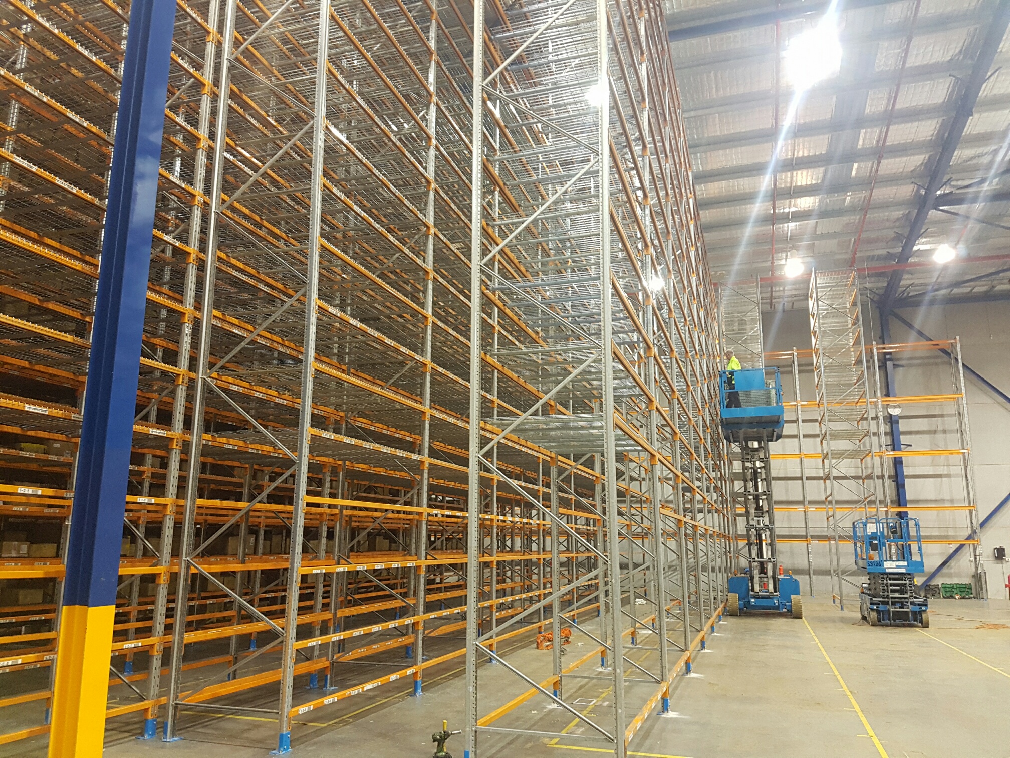 Pallet racking being installed by a person in a scissor lift.